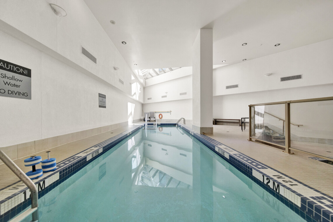 Indoor, empty swimming pool with tiled pools and lane markers; signs warn no diving, water calm and pale light from skylights above