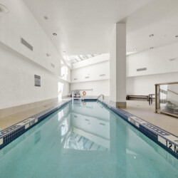 Indoor, empty swimming pool with tiled pools and lane markers; signs warn no diving, water calm and pale light from skylights above