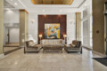 Lobby seating area with beige sofas, a colorful abstract painting centered on a dark wood wall, and two table lamps flanking the artwork in a bright lobby.