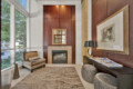 Elegant living room lobby with a wood-paneled wall, central fireplace, framed mirror, and seating arrangement with ottomans and chairs, low light glowing above.