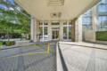 Entrance to a modern building with glass doors under a wide concrete canopy, brick columns, and yellow pickup/drop-off curb lines in the foreground.