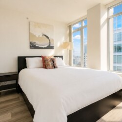 Bright hotel bedroom with a white bed, black wood headboard, and a small dark nightstand under a large abstract painting.