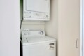 Stacked white washer and dryer in a narrow laundry alcove, with a doorway on the right side.
