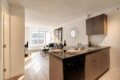 Open-concept kitchen with wood cabinets and island, set for two, adjacent living area with sofa and coffee table near a large window.