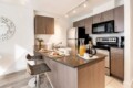 Modern kitchen with wood cabinets, an island, and a breakfast setup (pastries, coffee, and orange juice) for two under track lighting.