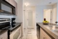 Modern kitchen with stainless steel stove, microwave, and coffee maker along a gray countertop wall; island with double sink and a bowl of fruit ahead.