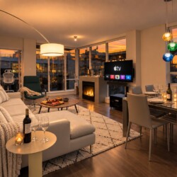 Modern open-plan living room with a white sofa, fireplace, and dining table set for a meal as sunset lights the room