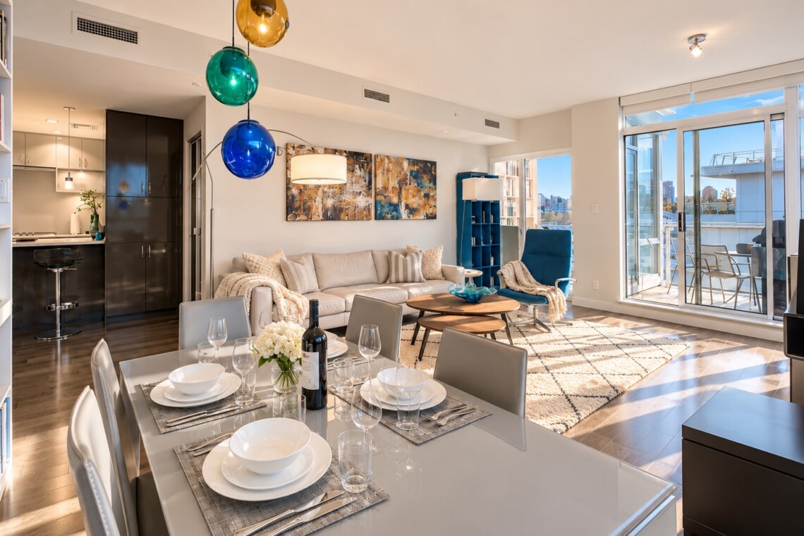Bright open-concept living and dining area with a white table set for six, a beige sofa, and colorful globe pendant lights on a sunny day.