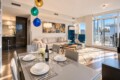 Bright open-concept living and dining area with a white table set for six, a beige sofa, and colorful globe pendant lights on a sunny day.