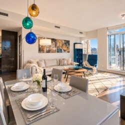 Bright open-concept living and dining area with a white table set for six, a beige sofa, and colorful globe pendant lights on a sunny day.