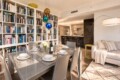 Open-concept living and dining area with a tall white bookshelf wall, a glass dining table set for six, and a beige sofa nearby.