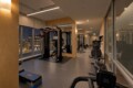 Modern gym interior at night with cable machines, weight racks, and mats, seen through large windows showing city lights outside.