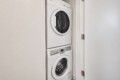 Stacked white front-loading washer and dryer in a narrow laundry closet with a white door open