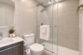 Modern bathroom with glass-enclosed shower, white toilet, and vanity; neutral beige tiles and potted plant.