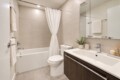 Modern bathroom with beige tiled walls, white bathtub with a shower curtain, toilet, and a dark wood vanity with a white sink.