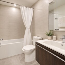 Modern bathroom with beige tiled walls, white bathtub with a shower curtain, toilet, and a dark wood vanity with a white sink.