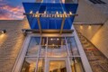 Facade of a modern building with a blue glass canopy and 'THE INDEPENDENT' sign over the entrance, sunset reflecting in glass, 2508 address visible