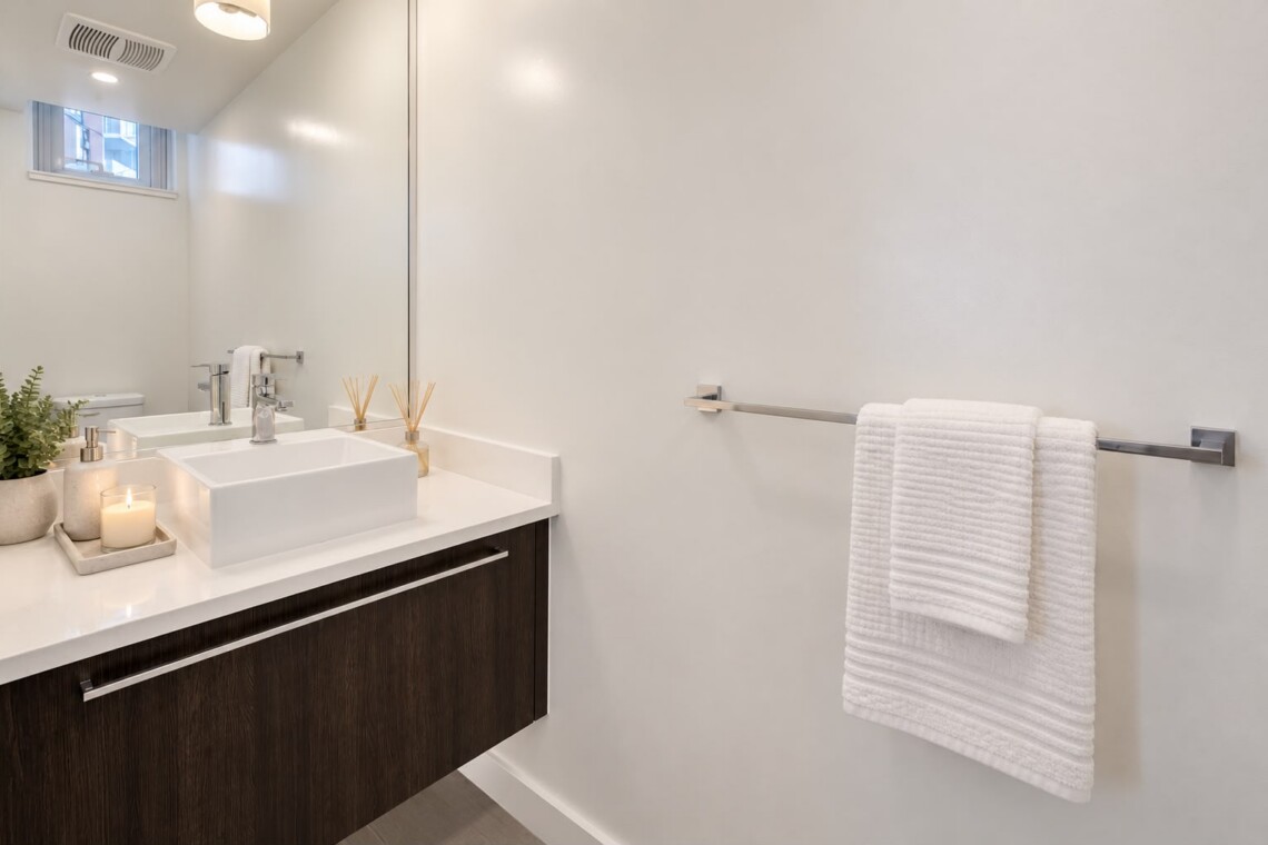 Modern bathroom vanity with a white square sink, dark wood cabinet, and a small plant on the counter.