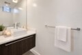 Modern bathroom vanity with a white square sink, dark wood cabinet, and a small plant on the counter.