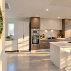 Modern kitchen with white and wood cabinets, stainless steel appliances, and a white island with bar stools under warm lighting.