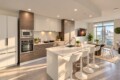 Modern kitchen with white and wood cabinets, island and bar stools, stainless steel appliances, and a dining area by large windows.
