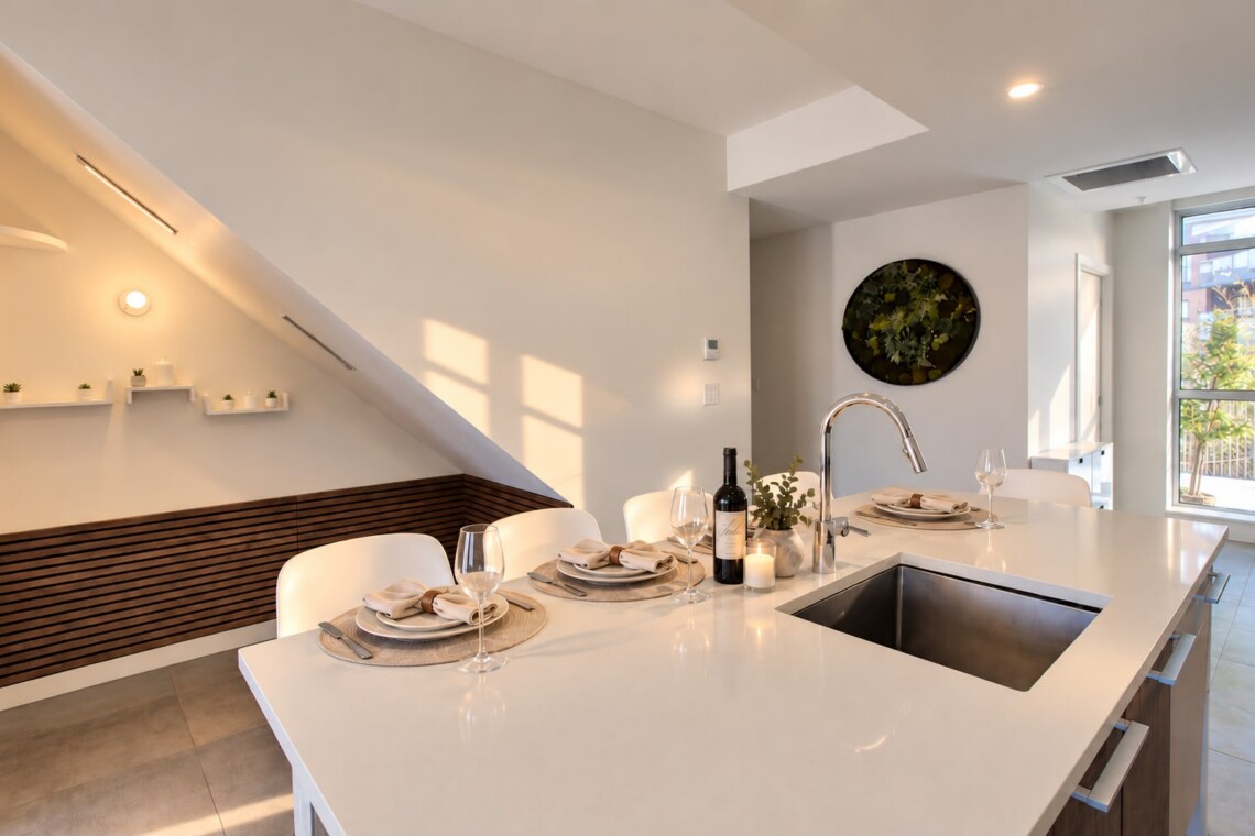 Modern white kitchen island set for four with wine, glassware, and napkins; stainless sink at center.
