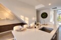 Modern white kitchen island set for four with wine, glassware, and napkins; stainless sink at center.