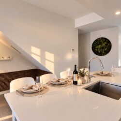 Modern white kitchen island set for four with wine, glassware, and napkins; stainless sink at center.