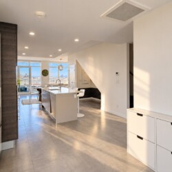 Bright, modern kitchen with a central island, white cabinetry, and bar seating, opening to a living area with city skyline views amid natural light.