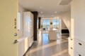Open-concept kitchen with white cabinets, an island, and bar stools, leading to large windows overlooking water and city skyline.