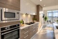 Modern kitchen with stainless-steel microwave and oven, white upper cabinets and wood-toned lower cabinets; sunlit balcony visible in the background.