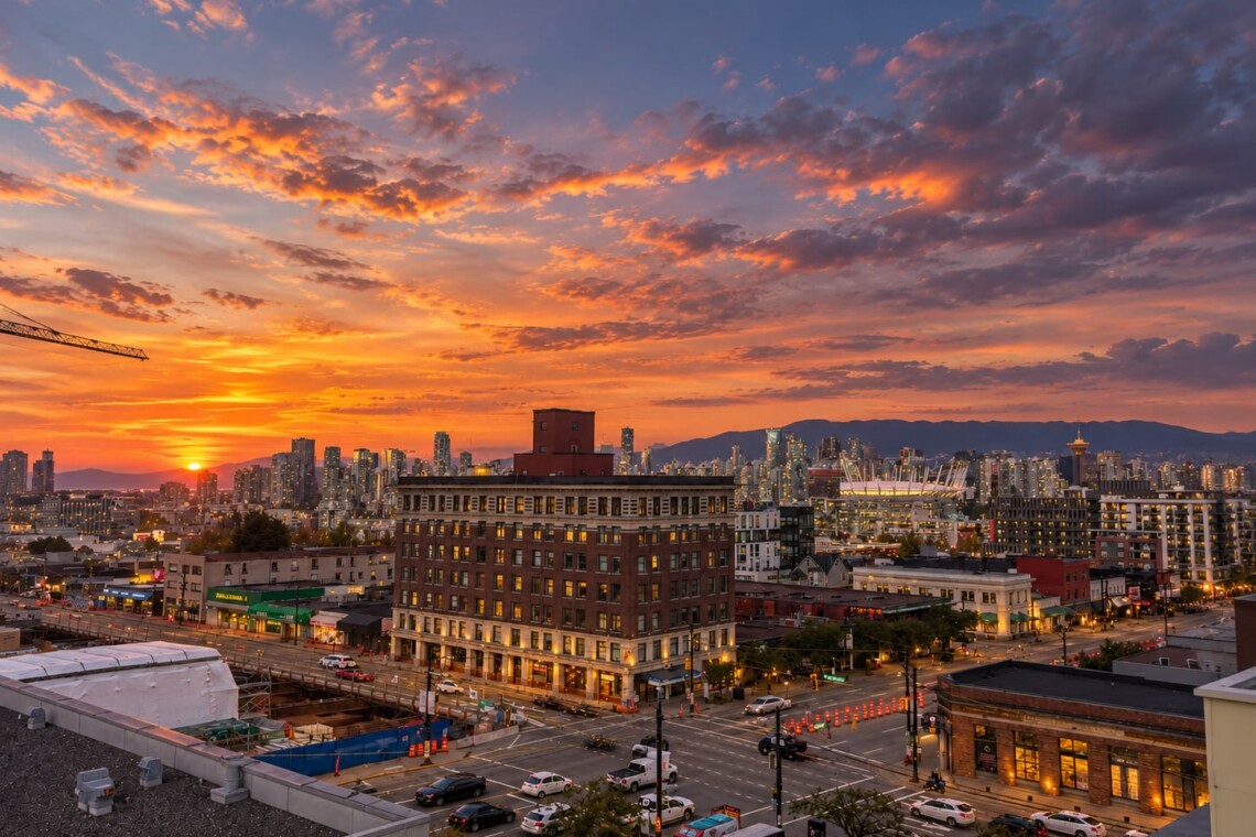 Sunset over a downtown area with orange clouds, a brick foreground building, and a busy street below.
