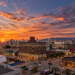 Sunset over a downtown area with orange clouds, a brick foreground building, and a busy street below.