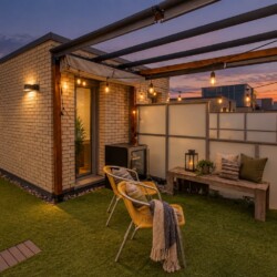 Rooftop patio at sunset with string lights, brick walls, and comfy seating on artificial grass.