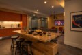 Modern kitchen and lounge with a long wooden island, chip bowls, drinks, and a wall-mounted TV showing a football game.