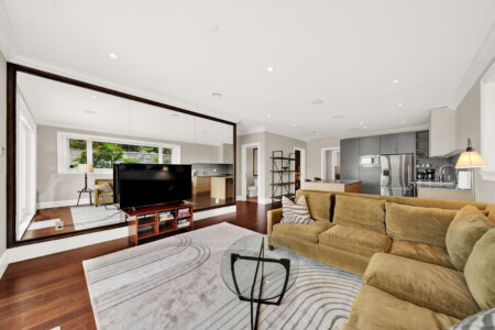 Open-concept living room with a beige sectional, glass coffee table, and a large wall-length mirror reflecting the TV.
