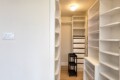 Bright walk-in closet with white built-in shelves, drawers, and a small black two-tier stool in the center of the room area.