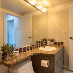 Bathroom vanity with granite countertop, oval sink, and mirrored wall reflecting a doorway with warm lighting.
