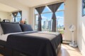 Modern bedroom with a dark gray bed and large window showing the city skyline; gray curtains pulled back.