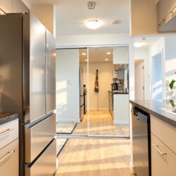 Open-concept kitchen with stainless steel refrigerator, stove, and island; warm sunlight casts shadows across the space.