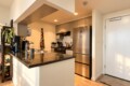 Modern kitchen with an island, stainless steel refrigerator, and a white entry door on the right.