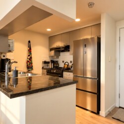 Modern kitchen with an island, stainless steel refrigerator, and a white entry door on the right.