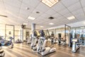 Well-lit gym interior with multiple cardio machines (treadmills and ellipticals) and weight machines arranged in rows.