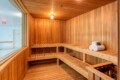 Wooden sauna with multi‑level benches, rolled white towels on the right, and a small ceiling light.