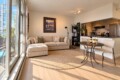 Open-plan living room with a beige sectional sofa, round rug, and a small dining table set for two; kitchen in the background.