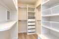 Walk-in white closet with built-in shelves, drawers, and hanging rods, plus clear plastic storage bins on the right side.