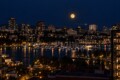 Full moon over a nighttime city skyline with a marina of docked boats and warm city lights reflecting on the water.