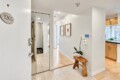 Foyer of an apartment with a 1205 plaque, mirrored wall, wooden bench, and a white orchid plant on a small table edge.