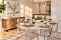 Round marble dining table set for six with clear acrylic chairs, wine bottles, candles, and a succulent centerpiece in a sunny modern dining area