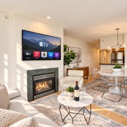 Open living room with Apple TV above a gas fireplace, beige sofa, and marble coffee table with wine."','Sunlit round marble dining table with clear chairs and a modern chandelier; kitchen in the background."','Tall windows, neutral tones, potted plant, and patterned area rug under seating."','Wine bottle and two glasses on a marble coffee table in a bright contemporary living space."','Neutral-toned living/dining area with plants, artwork, and a cozy fireplace.